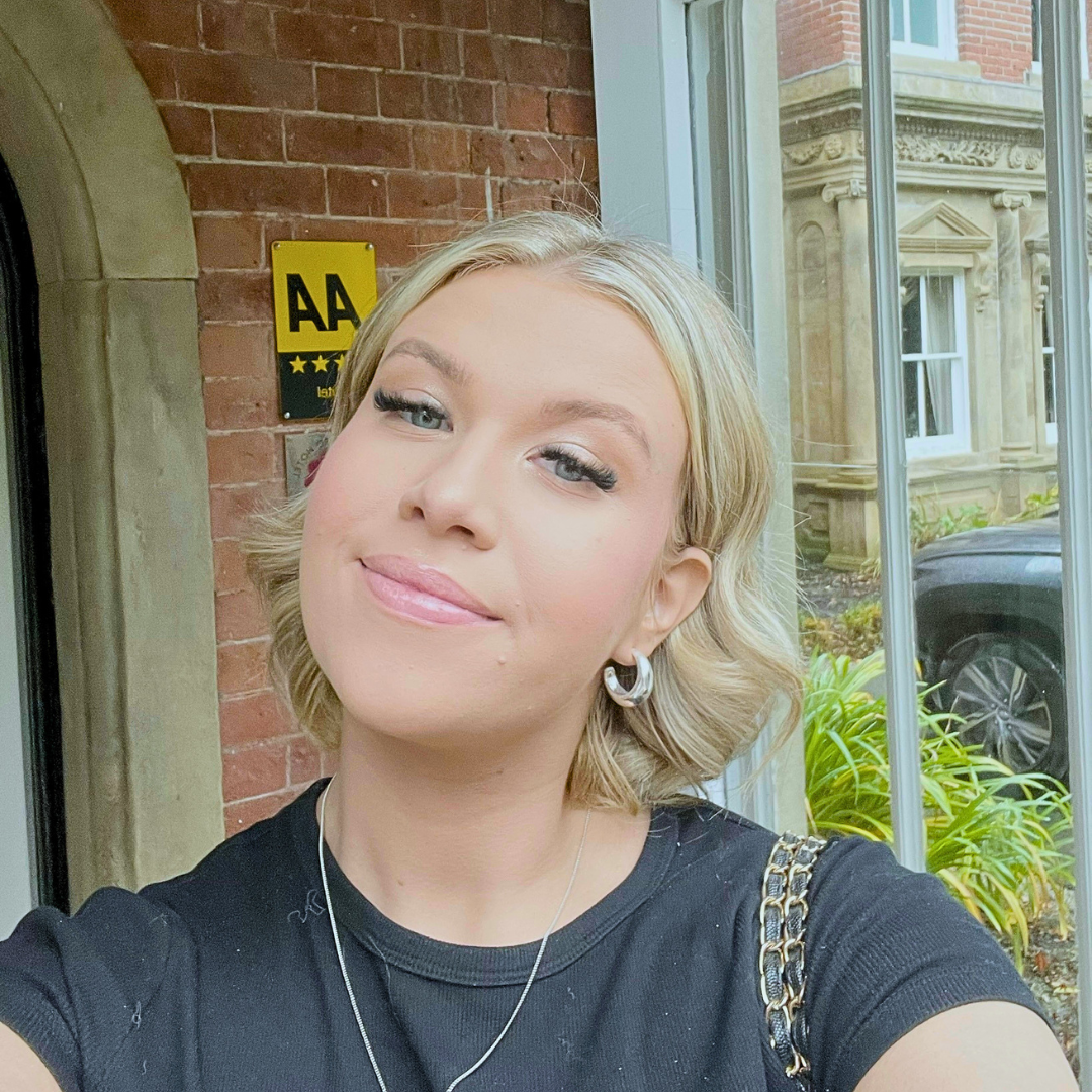Photo of woman with blonde hair and a black top on. in front of a building with bricks and glass.